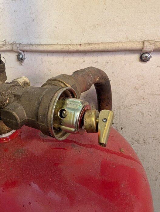 Expansionskärl med två ventiler, en vit där vatten sipprar ut och en annan som släpper ut luft, mot grå vägg.