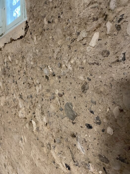 Rå betongvägg med småsten, delvis skadad yta vid ett fönster. Vägg från 1930-talet i en källare, redo för kalkputsning.