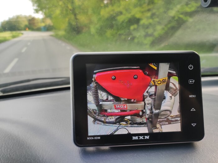 Kamera på bilens instrumentbräda visar livebild av en mopeds sidoväska och fjädring genom bakrutan.