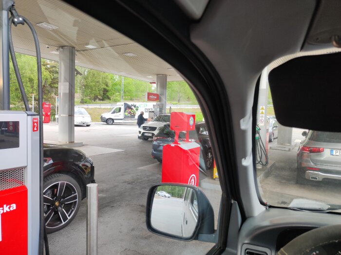 Bilar parkerade vid bensinpumpar på en bensinstation, ingen synlig aktivitet vid pumparna.