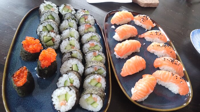 Hemlagad sushi med nigiri toppad med lax och rullar med gurka och lax, samt bitar med röd rom på två fat.