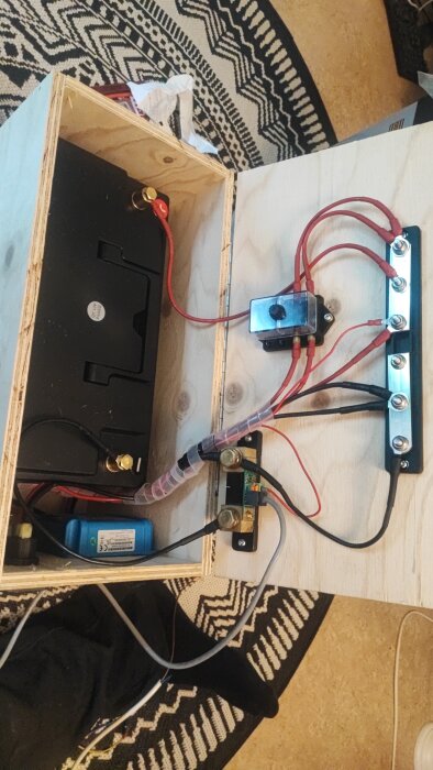 Träkista innehållande batteri och elektroniska komponenter med flera anslutna kablar och terminaler.