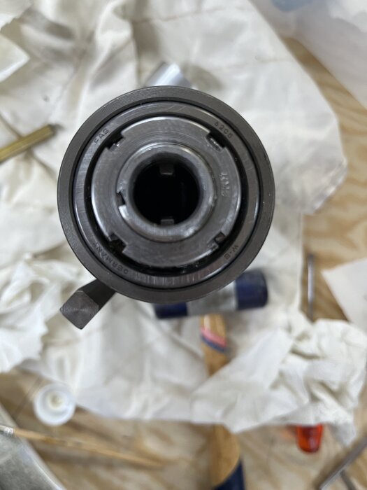 Spindelhylsa med två kilspår på en arbetsyta; bakgrunden har verktyg och material.