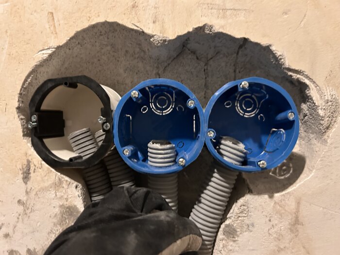 Tre eldosor i en vägg, två blå och en vit, anslutna med korrugerade rör. Ett av rören hålls på plats. Förberedd för fuktsensorinstallation.