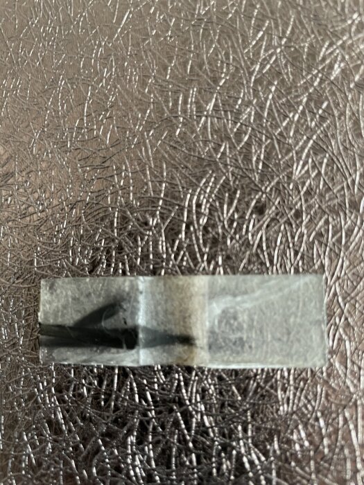 Genomskinlig tejp fastklistrad på en yta med silverfärgat, texturerat mönster.