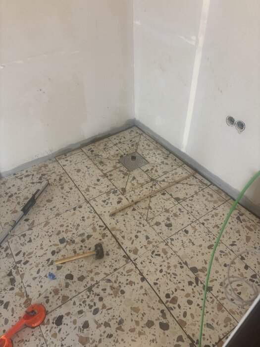 Golvyta med terrazzo-plattor, verktyg som hammare och vattenpass ligger på ytan. Väggar runt om väntar på vidare renovering.