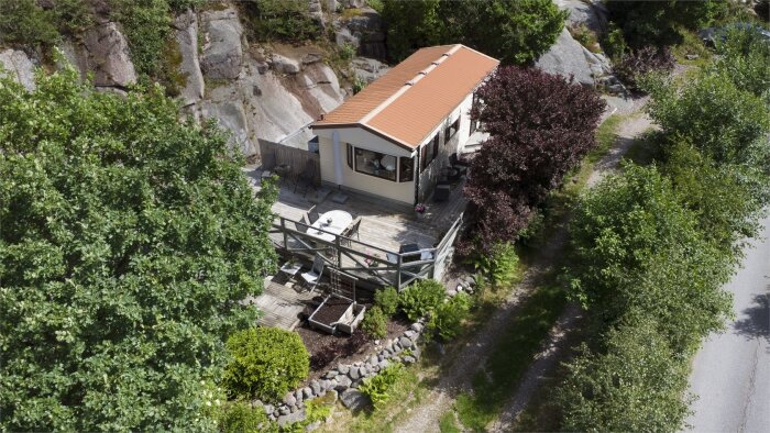 Bild av en villavagn med stor terrass av tryckt virke, omgiven av grönska och belägen vid en klippig sluttning i Kungshamn.
