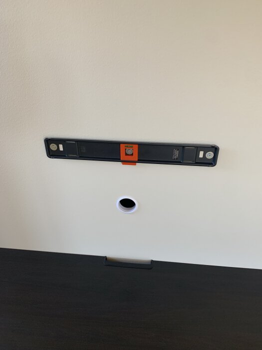 Vägg med monterad tv-fäste och vattenpass över en cirkulär kabelgenomföring i gipsskiva.