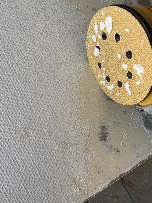 Slippapper på slipmaskin med klumpar av färg och material på garderobsdörr med övermålad vävtapet, synligt problem vid bortslipning.
