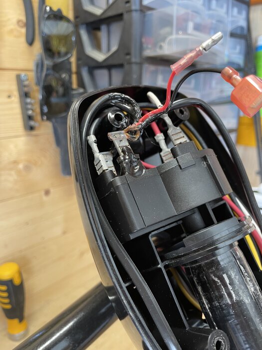 Brända kablar i en elektrisk båtmotor med några synliga kopplingsstycken och plastkåpa, eventuellt överhettningsskada i motorrummet.