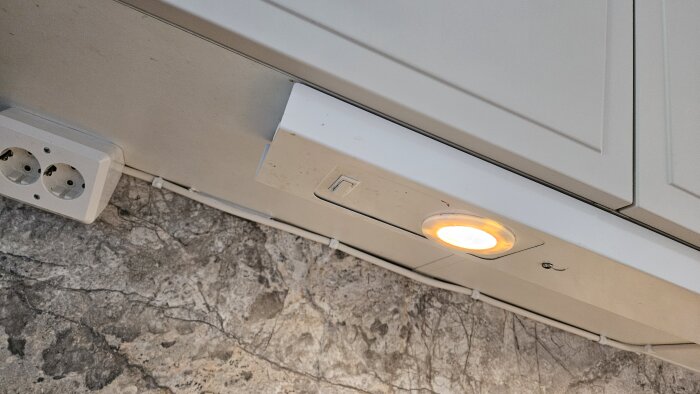 Bänkarmatur med lysande lampa under skåp, intill eluttag.