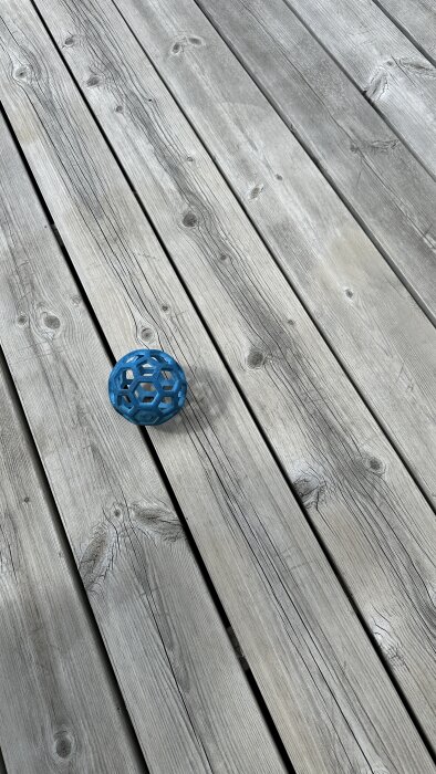 Grå trallbrädor på en altan med en blå boll ovanpå, som ser välskött ut efter endast tvätt med vatten sedan 2018.