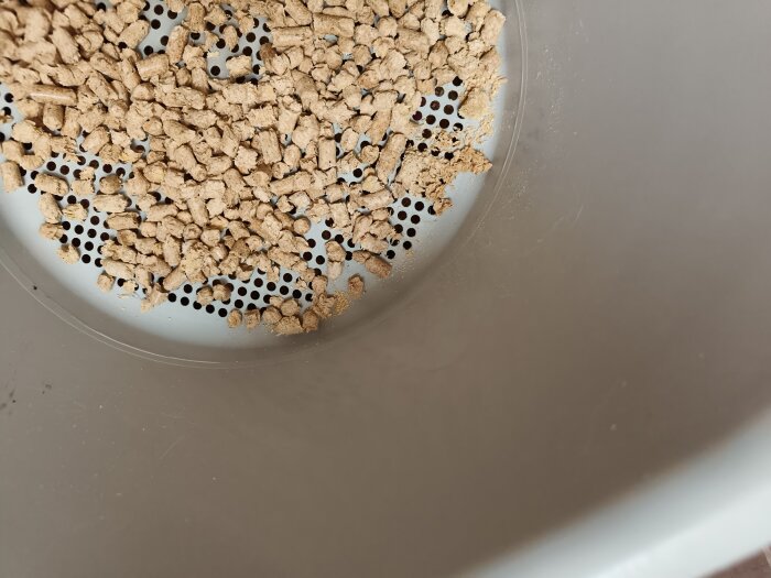 Pellets i en kattlåda med hålat botten, alternativ till traditionell kattsand. Miljövänligt och minskar damm och soptaxa.