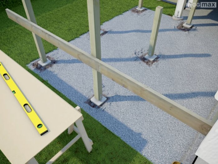 Trästolpar monterade i stolpskor på en grusyta med en bärlina i trä och ett arbetsbord med ett vattenpass i förgrunden.