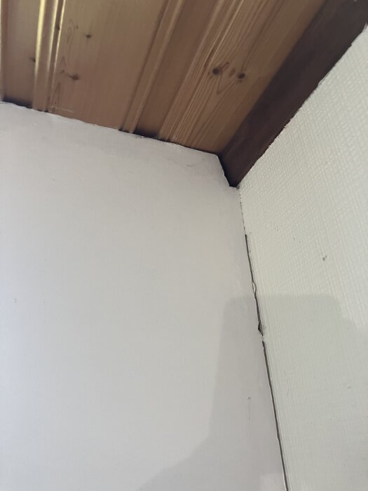 En närbild av ett hörn där vägg möter tak med träpanel och en liten spricka i hörnet.