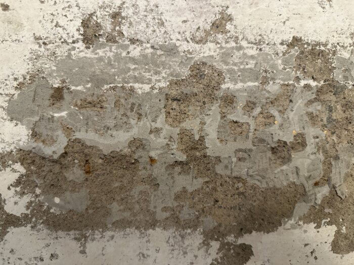 Vägg med spackel- och kalkfärgslager där betongliknande material syns under, visar ytan efter att vävtapet tagits bort i en 20-talshuskällare.