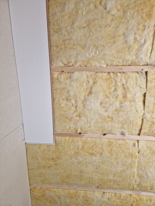 Isolering ovanpå ett tak med träreglar synliga mellan isoleringsmaterialet.