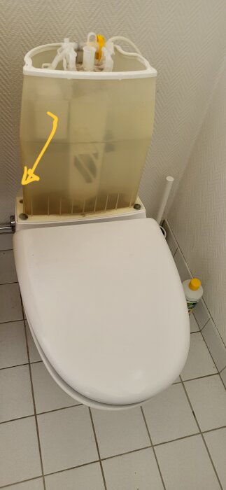 Ifö toalettstol med läckage vid skruvhålet till vänster under vattenbehållaren. Skriven textanvisning pekar mot läckageområdet.