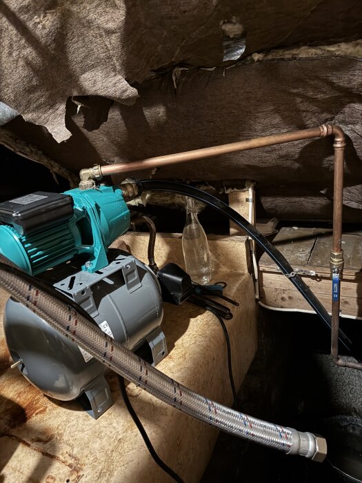 Hydroforpump med anslutna kopparrör och en flexibel anslutningsslang. Bakgrund visar isolerad väggyta och olika verktyg på bänken.