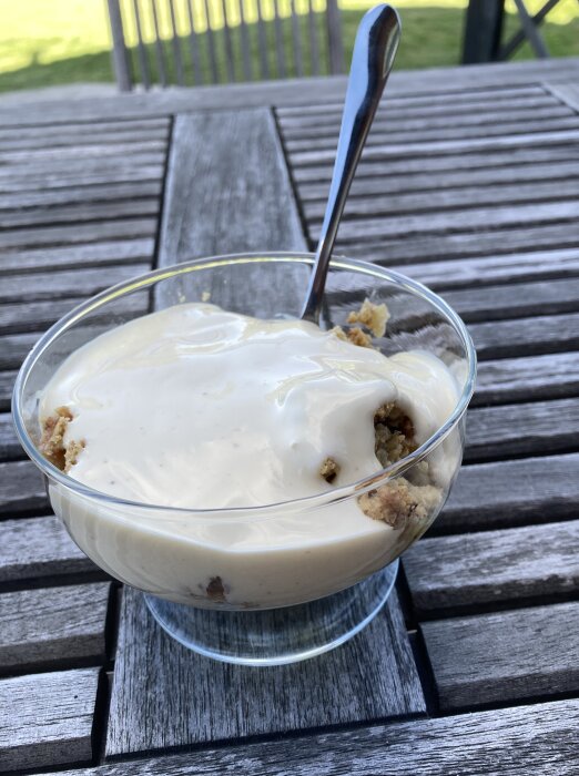 Skål med rabarberpaj toppad med vaniljsås på ett träbord utomhus.