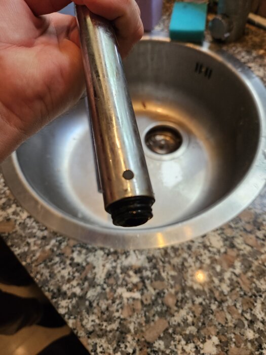 Hand håller avbruten köksblandarens pip över en diskbänk.