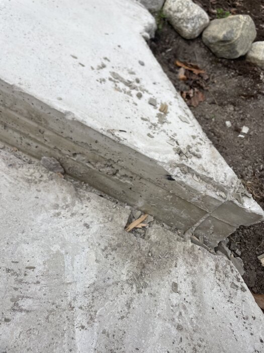 Ojämn och sprucken yta på en nyligen byggd betongtrappa utomhus, omgivna av stenar och jord.