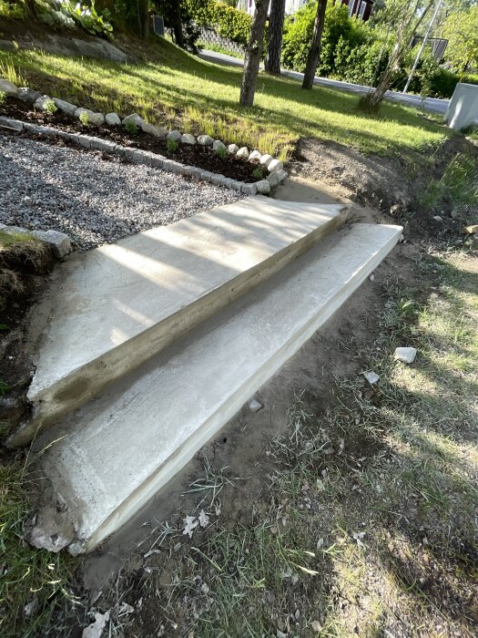 Utomhustrappa i två steg med ojämn yta och små sprickor, omgiven av gräs och stenar.