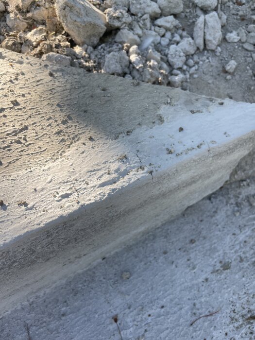 Ojämn betongyta med synliga sprickor och färgskiftningar på en utomhustrappa, omgiven av grus och små stenar.