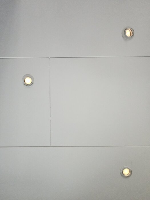 Vitt slätt innertak med rektangulära takpaneler och infällda spotlights.