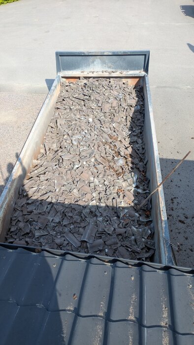 Container fylld med krossade takpannor i soligt väder, efter takrenovering.
