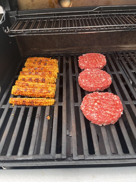 Majskolvar och råa hamburgaregrytor på en grill.