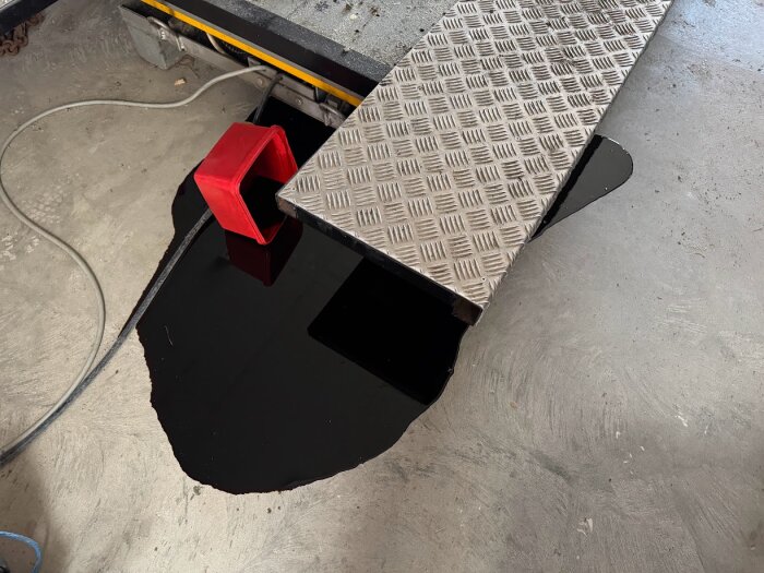 Spillolja på garagegolv bredvid en upphöjd ramp, med en röd balja på sidan.