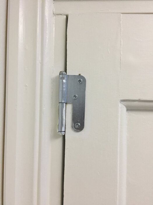 Dörrgångjärn på vitmålad trädörr och dörrkarm, närbild.
