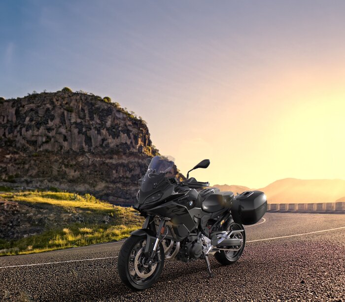 BMW 900XR motorcykel på en landsväg vid solnedgången, med berg i bakgrunden.