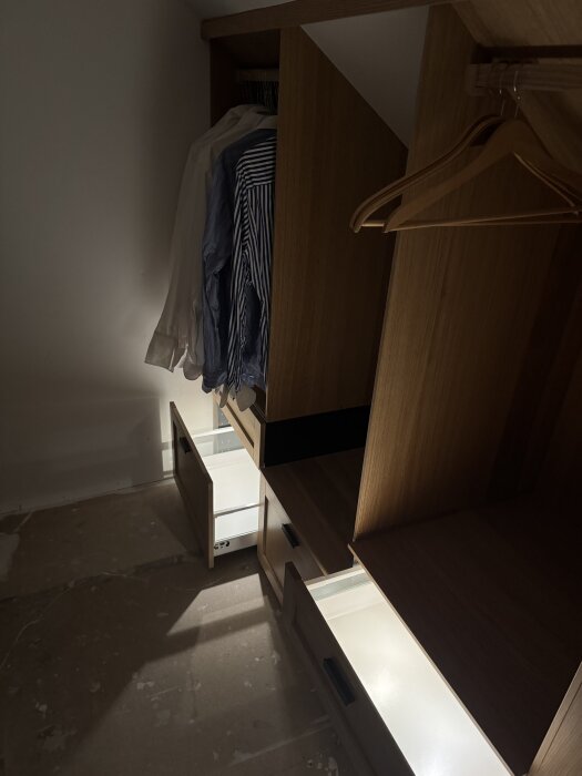 Walk-in-closet med Metod-stommar, inbyggda lådor och integrerad belysning. Kläder hänger på galgar, rummets snedtak syns.
