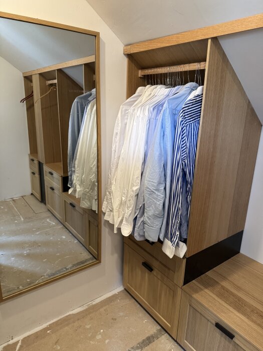 Walk-in-closet med snedtak byggd av Metod-stommar; skjortor hänger på galgar, lådor undertill, försedd med spegel och trädetaljer.