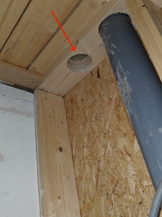 Tak med hål för ventilationsrör i ett isolerat bjälklag, med en röd pil som pekar mot hålet.