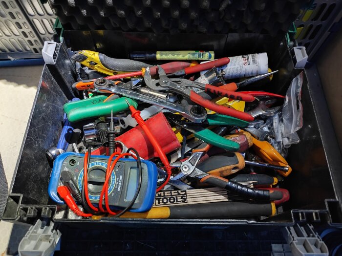 Verktygslåda med olika verktyg som tänger, skiftnyckel, skruvmejslar och en multimeter, allt huller om buller.