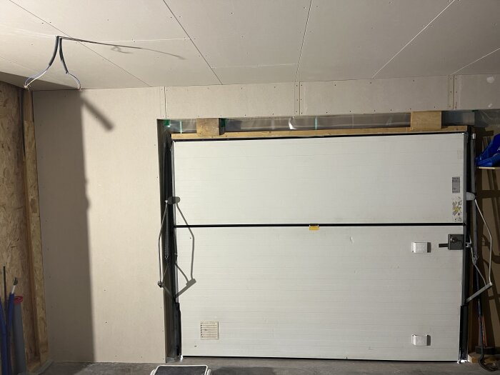 Inre väggar klädda med gipsskivor, garageport synlig, taket har oskyddade elektriska ledningar.