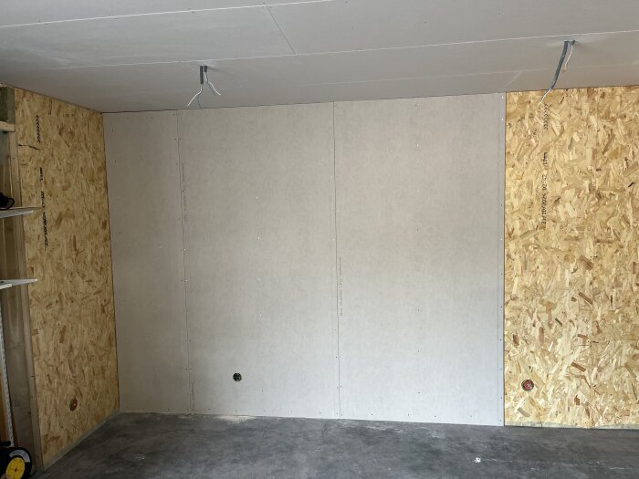 Vägg med monterade gipsskivor och OSB-skivor, färdiginstallerade eluttag och lösa elsladdar i taket för kommande arbete.