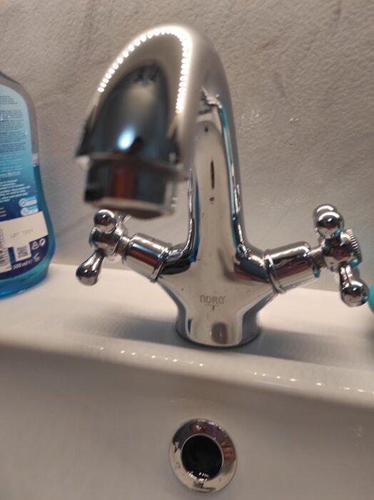 Kromfärgad vattenkran med två vred, placerad ovanpå en vit handfat.