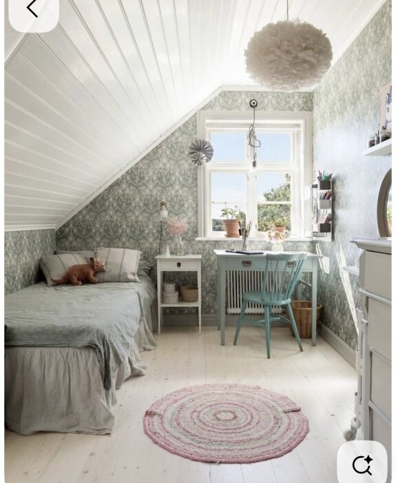 Ett sovrum med snedtak och hålkälspanel. En säng, matta, skrivbord och stol är arrangerade harmoniskt. Ljuset strömmar in genom ett stort fönster.