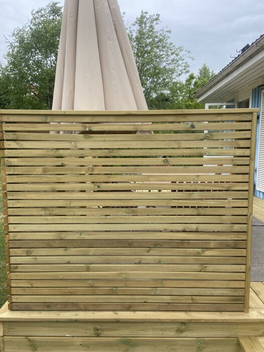 Träribbor på altan med några böjda ribbor som går ihop, mot en bakgrund av träd och en parasoll.