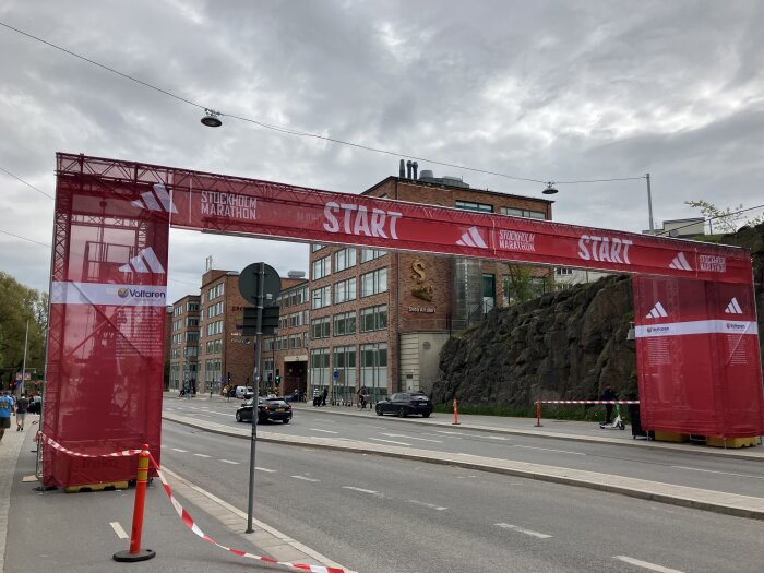 Startlinjen för Stockholm Marathon med en röd bannér över gatan. I bakgrunden syns moderna byggnader och en bergsvägg.