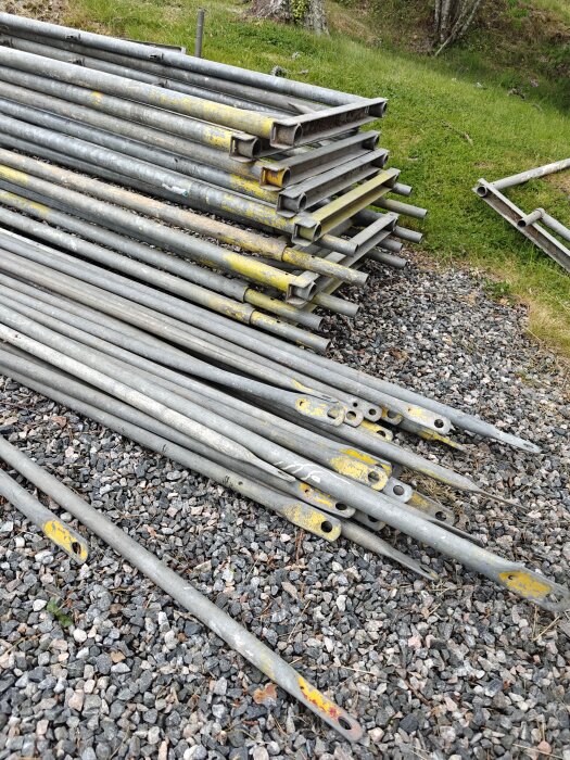 Hög av byggnadsställningsdelar liggande på en grusplan.