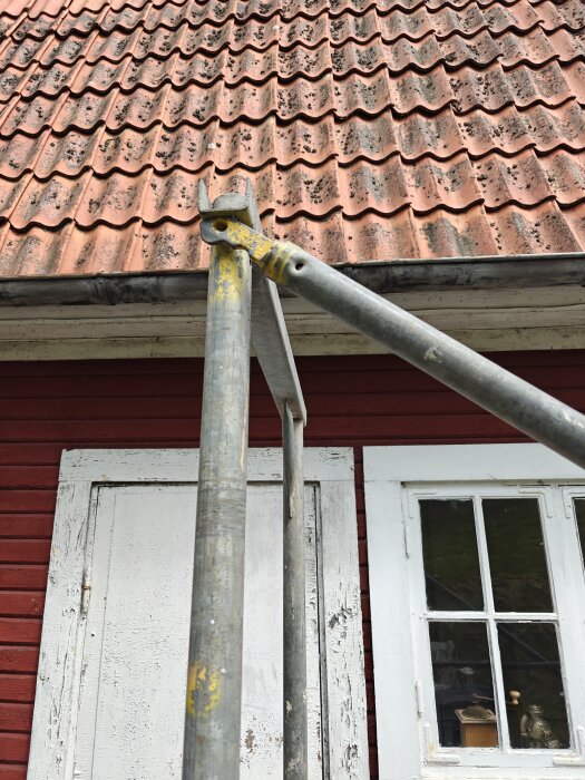 Byggnadsställning mot rött hus med tegelpannor.