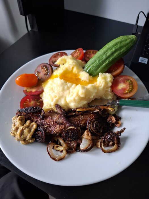 Tallrik med potatismos toppat med äggula, stekt sidfläsk med lök och senap, samt gurka och tomater.