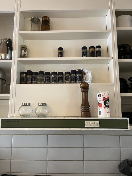 Gammal köksfläkt från 1971 med Husqvarna-märke. Fläkten är monterad under ett skåp och omgiven av kryddor och köksinredning.