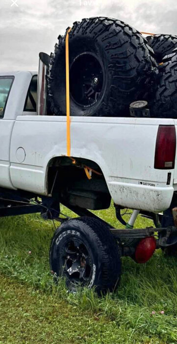 Pickuptruck utan bakhjul med stora terrängdäck i flaket, orange spännband säkrar lasten.