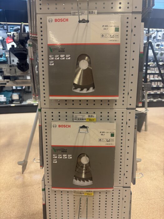 Förpackningar med Bosch cirkelsågklingor hänger på ett ställ i ett byggvaruhus, med olika storlekar och priser synliga.